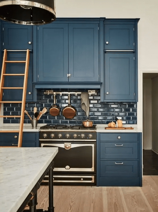 A vintage-style navy blue kitchen with glossy navy subway tiles, white marble countertops and metallic accents