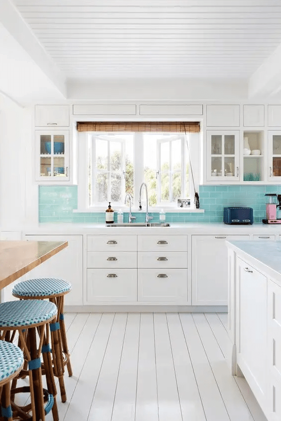 a white coastal kitchen with shaker cabinets, a turquoise subway tile backsplash, a stained table, and blue stools