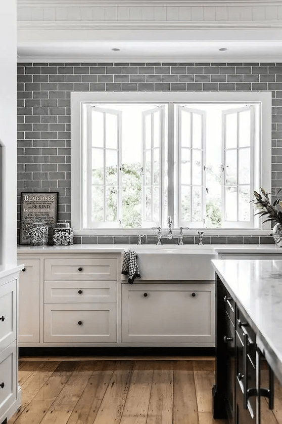 A white farmhouse kitchen with gray subway tiles along the entire kitchen wall and white stone countertops is a chic space