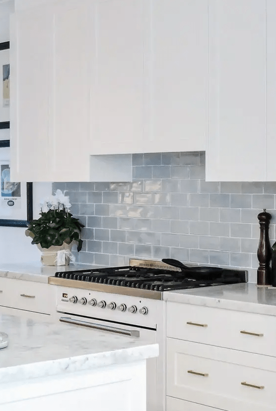 a white farmhouse kitchen with white countertops, a gray subway tile backsplash, and gold fixtures