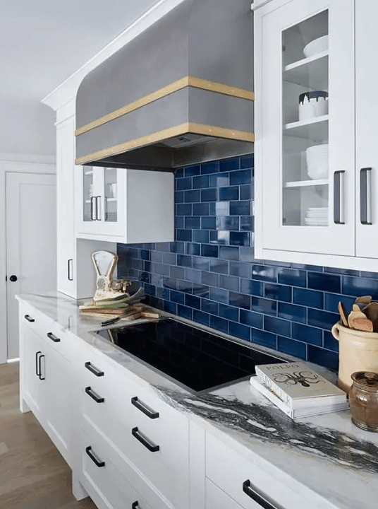 A white kitchen with a navy subway tile backsplash, metal hood, and white stone countertop is super chic