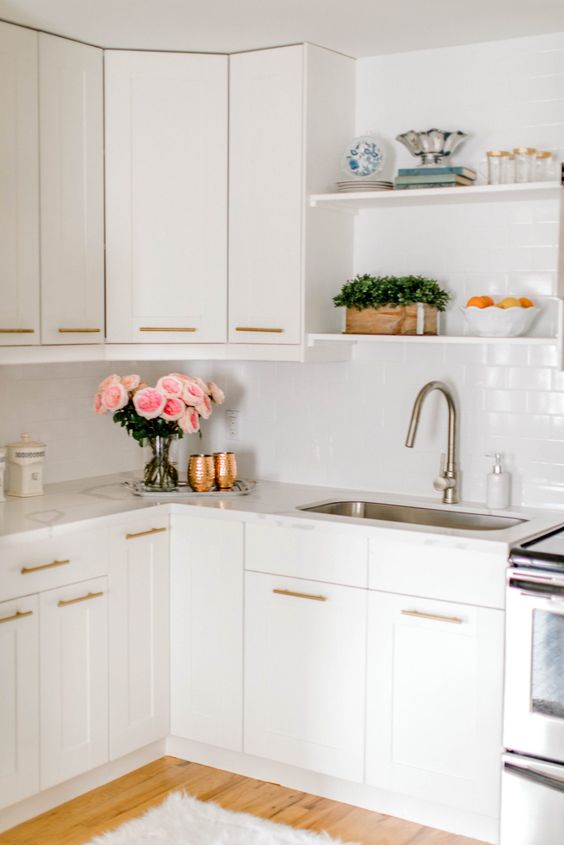 A white kitchen with a white subway tile backsplash and white countertops and gold fixtures is a beautiful space
