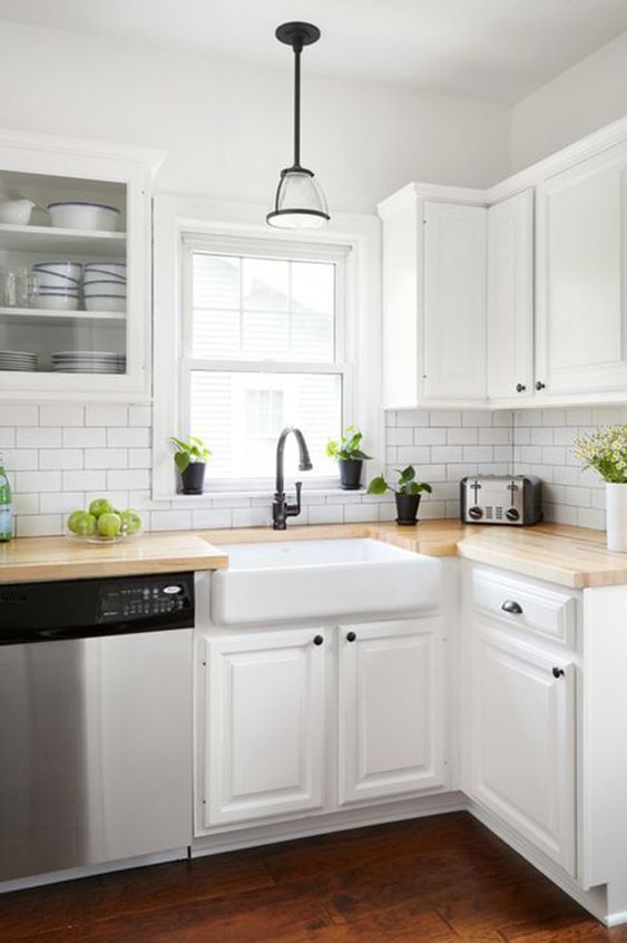 A white modern farmhouse kitchen with butcher block countertops, white subway tile, and black accents for contrast