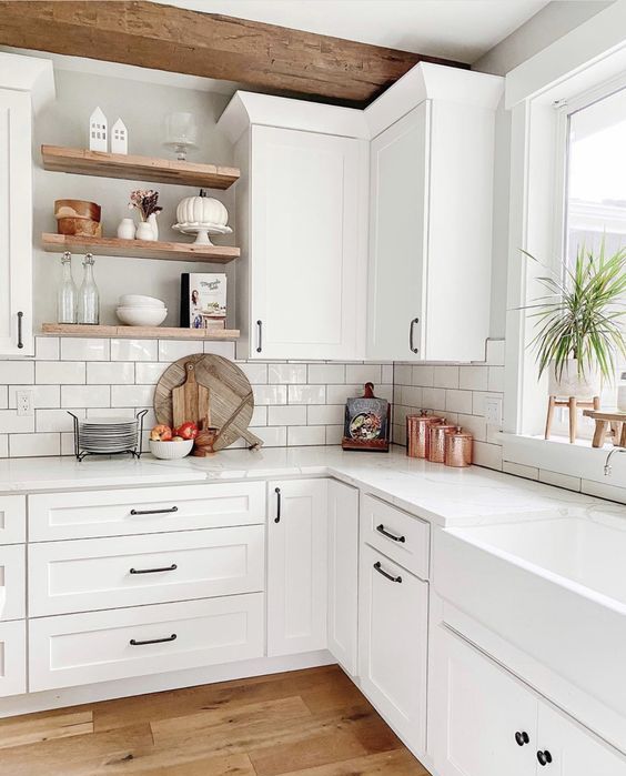 a white modern farmhouse kitchen with shaker cabinets, white stone countertops and a white subway tile backsplash and stained wood