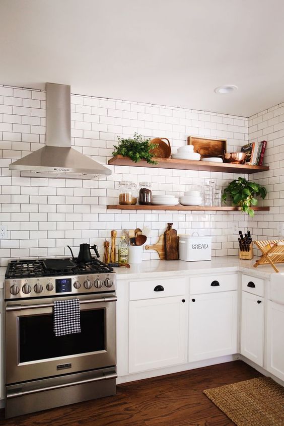 a white, modern farmhouse kitchen with stained corner shelves and white subway tiles on the walls