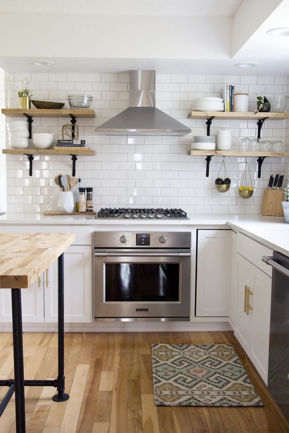 A white modern farmhouse kitchen with white countertops, stained shelves and an island with gold handles