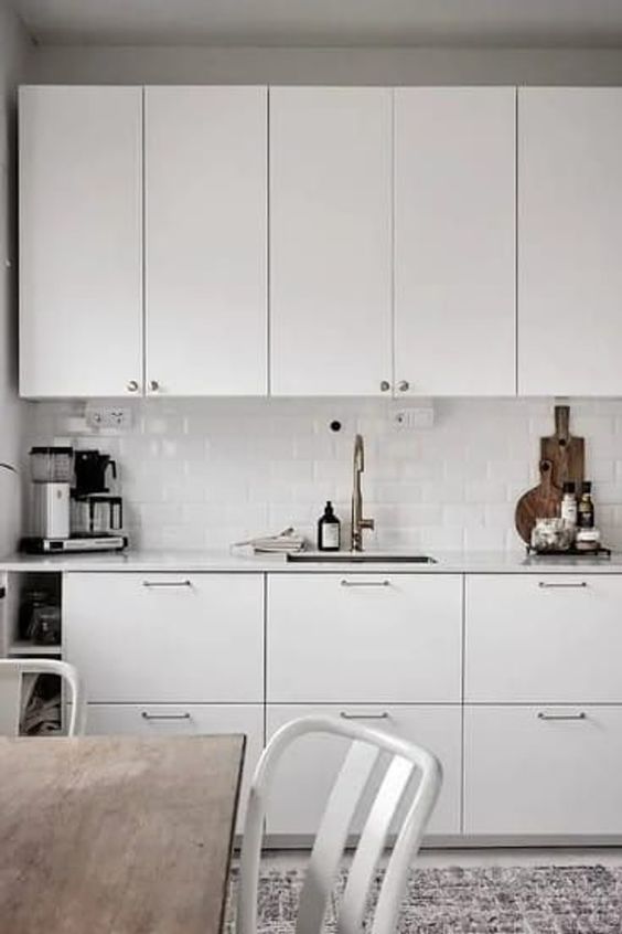 a white Nordic kitchen with white countertops and a white subway tile backsplash and simple dining room furniture