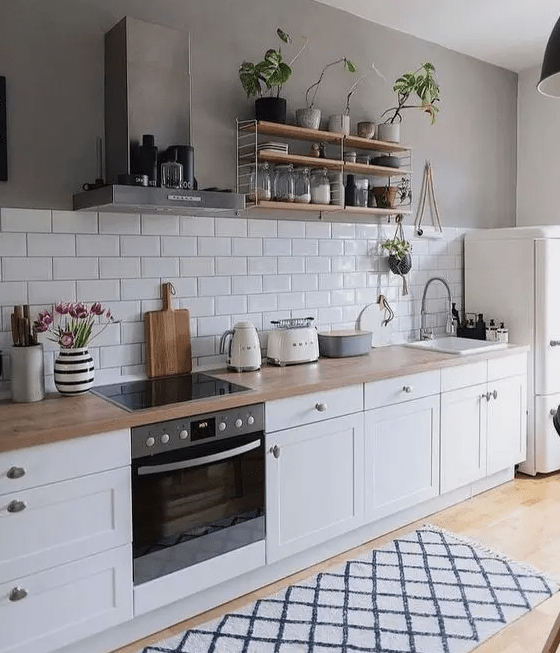 a white Scandinavian kitchen with shaker cabinets, butcher block countertops, a white subway tile backsplash, and open shelving