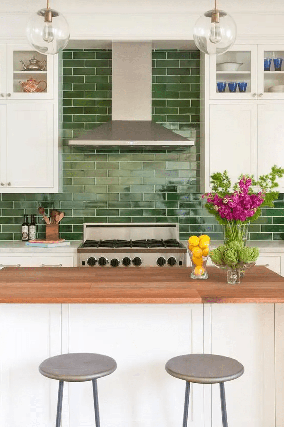 A striking white farmhouse kitchen with stone and butcher block countertops and a striking green subway tile backsplash
