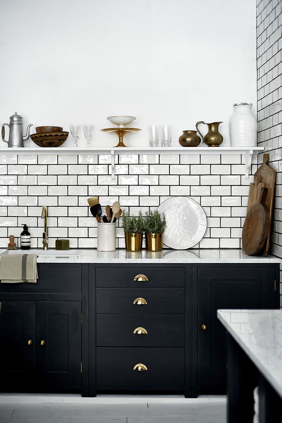 A bold black kitchen with a white subway tile backsplash accented with black grout and touches of gold and brass
