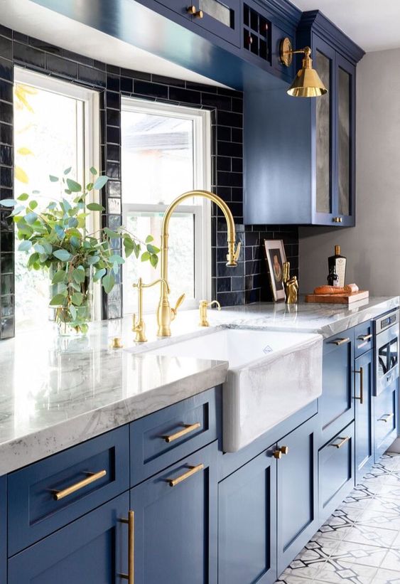 A bold blue kitchen with a black subway tile backsplash, white marble countertops and lots of gold for a polished vibe