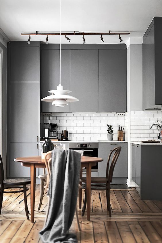 A minimalist gray kitchen with white countertops and white subway tiles as well as a wooden dining set looks very inviting