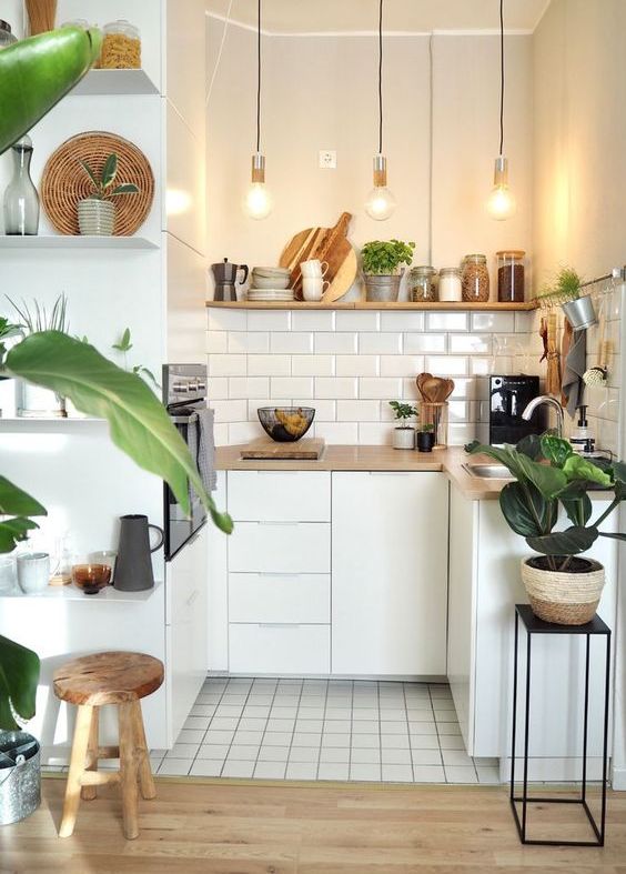 A small, minimalist white kitchen with wooden countertops and shelving, as well as a white subway tile backsplash and hanging lamps
