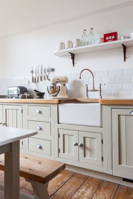 A light green vintage kitchen with large format subway tiles, wooden countertops and a traditional dining set with benches for a country atmosphere