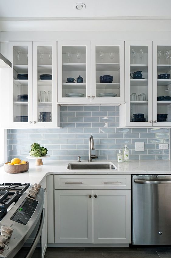 An airy white kitchen with a light blue subway tile backsplash and neutral metallic colors looks very inviting