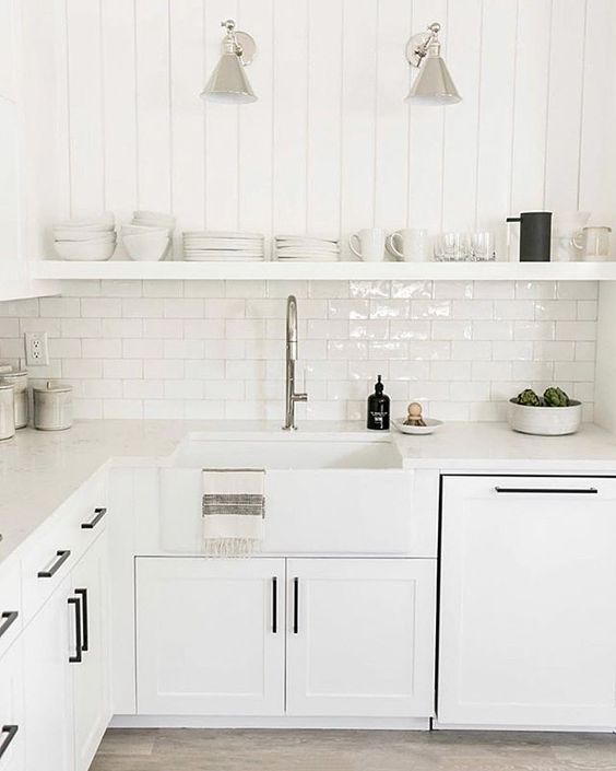 an ethereal white kitchen with shaker cabinets, white countertops, open shelving and black fixtures