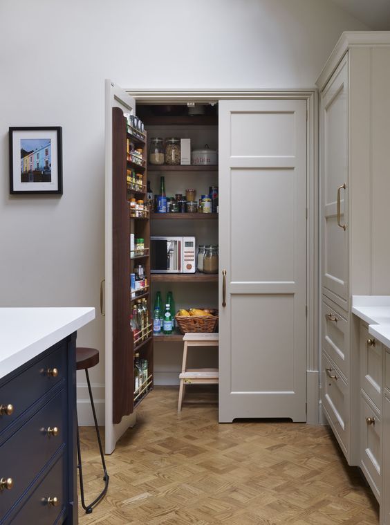 a cool and small pantry with shelves on the doors and inside, with a stool and baskets for storage