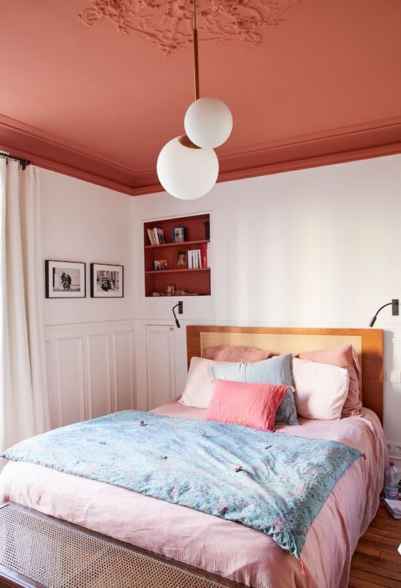 a modern bedroom with a red ceiling, an alcove with shelves, a bed with pink linens and some artwork and lamps