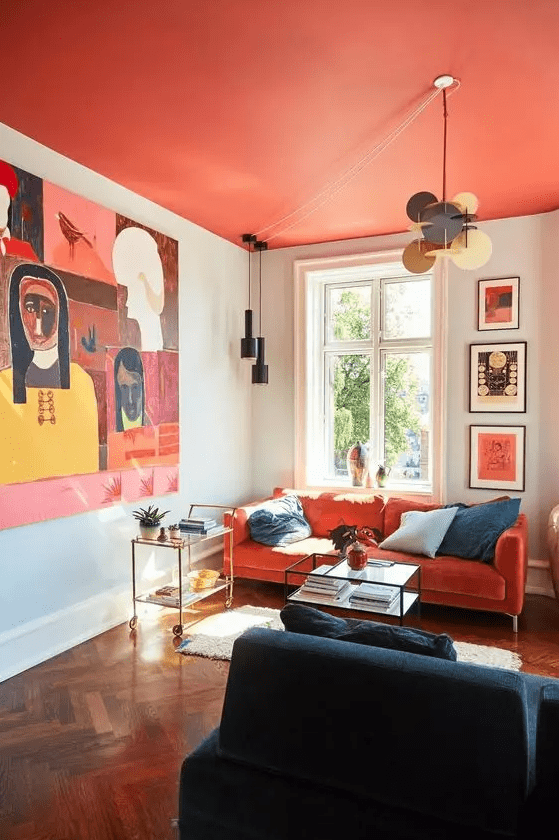 a bright living room with a bright red ceiling, an orange sofa, a navy blue chair, eye-catching artwork and pendant lamps, and elegant coffee tables