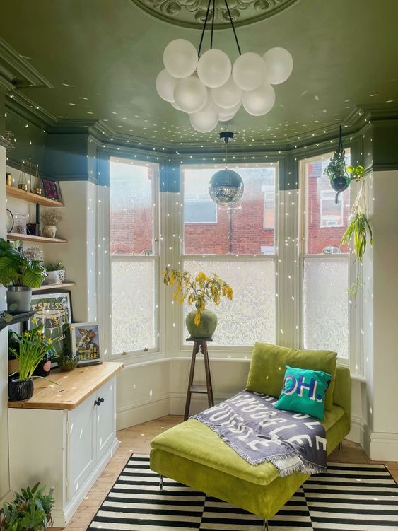 a pretty bay window room with a green ceiling, a closet and shelves with art, a green daybed and a striped rug, and a disco ball