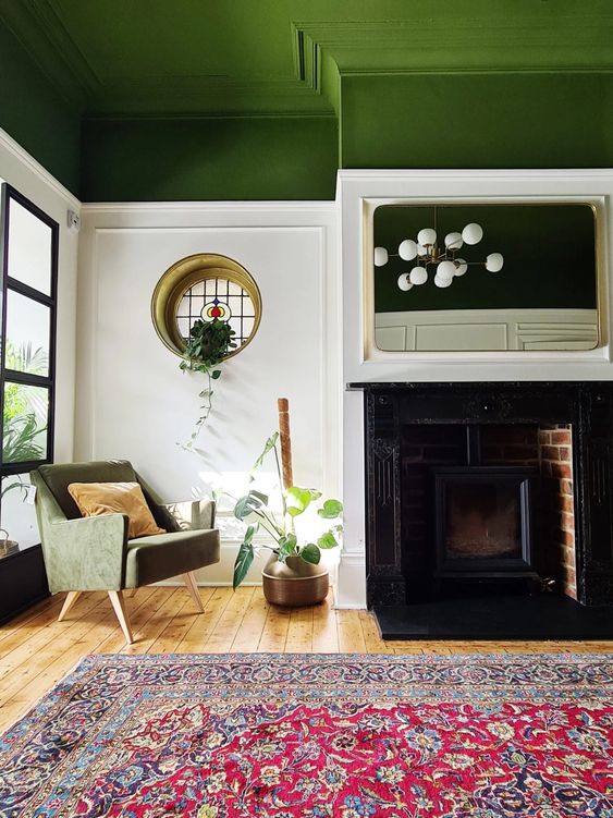 a striking living room with a green ceiling, a fireplace, a green chair, a round window, a bold printed rug and a potted plant