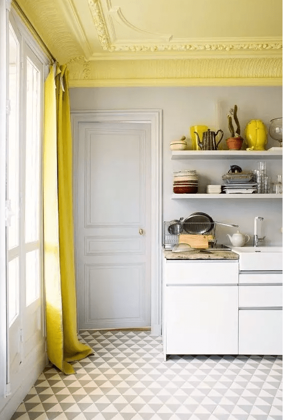 A neutral kitchen accented by a yellow stucco ceiling, a yellow curtain and a printed rug, as well as some yellow accents