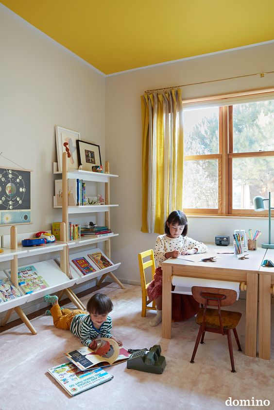 a playroom with a yellow ceiling, a desk with boards and open shelves, a large rug and yellow striped curtains