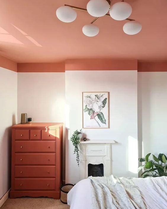 a neutral, bright bedroom with a coral ceiling and matching dresser, a small fireplace, a bed and some greenery