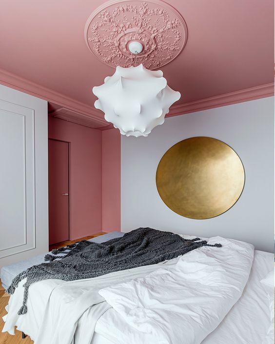an elegant bedroom with a pink blanket, a bed with neutral linens, a large brass circle as a piece of art and a beautiful cloud chandelier