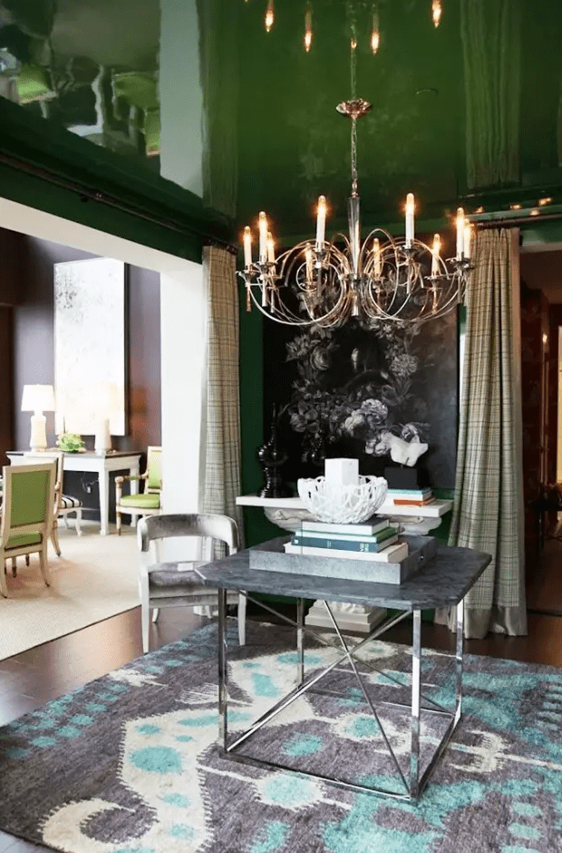 an elegant entryway with a glossy green ceiling, dark artwork, a console and coffee table, a chic chandelier and a bold printed rug