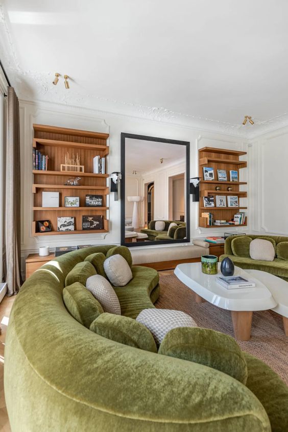 A living room with built-in bookshelves, a large mirror and bench, green curved sofas and coffee tables is amazing
