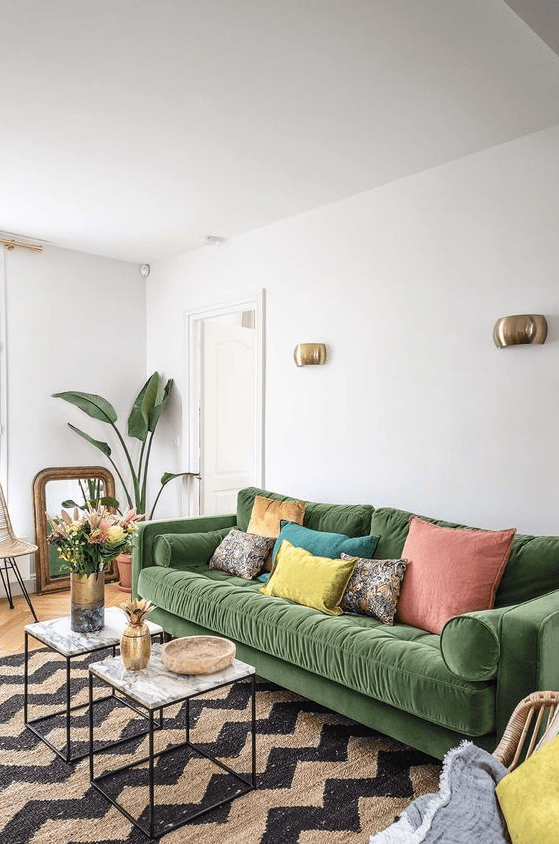 a colorful living room with a green sofa and light cushions, a chevron rug, coffee tables, brass elements and potted plants