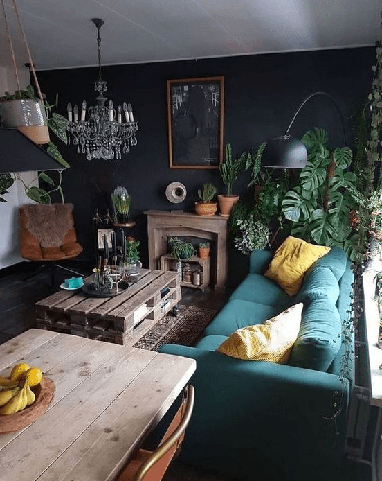 a moody, eclectic living space with a teal sofa, leather armchair, colorful cushions, crystal chandelier and pallet coffee table