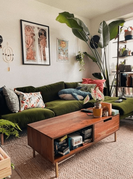 A mid-century modern living room with a green seating area, coffee table, statement plants, decor and a shelf