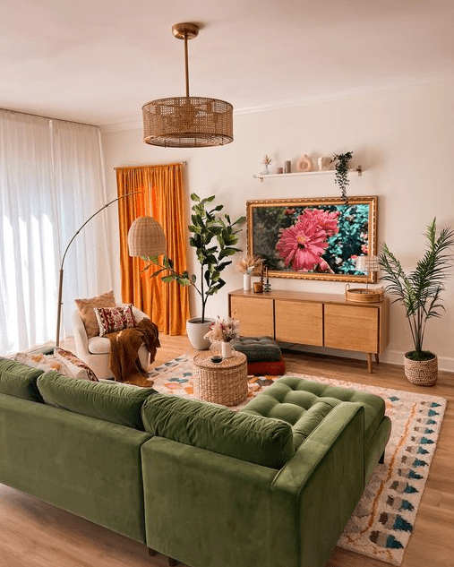 a cozy living room with a green sofa, a rug, a curved sofa, a side table, a TV, a woven chandelier and potted plants