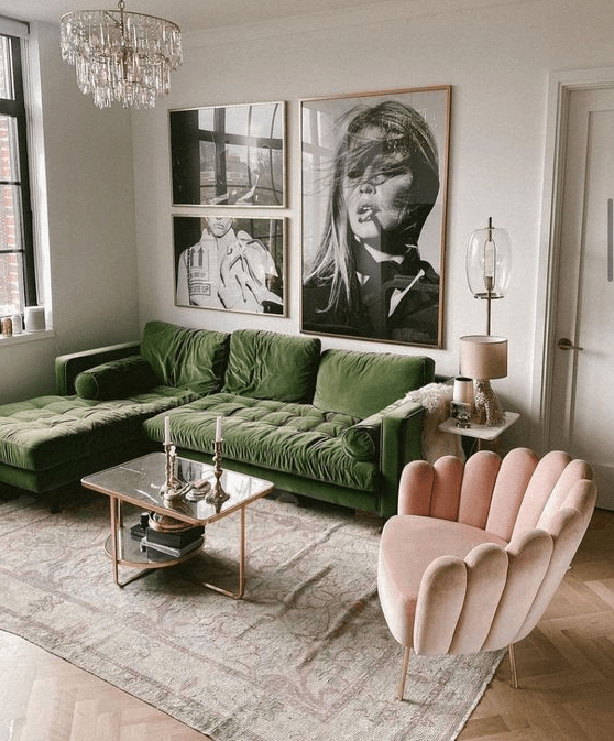 a chic living room with a green sofa, a pink curved chair, a coffee table, a gallery wall and a chandelier