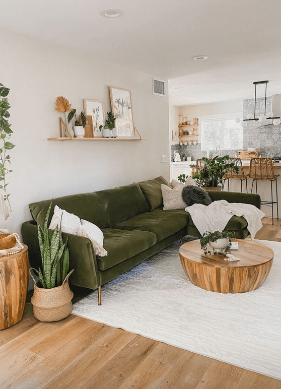 a modern, neutral living room with a dark green accent sofa, potted plants, a coffee table and a wall of shelves