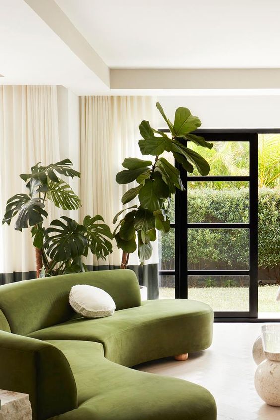 a modern living room with a green curved sofa, potted plants, color block curtains and an entrance to the garden