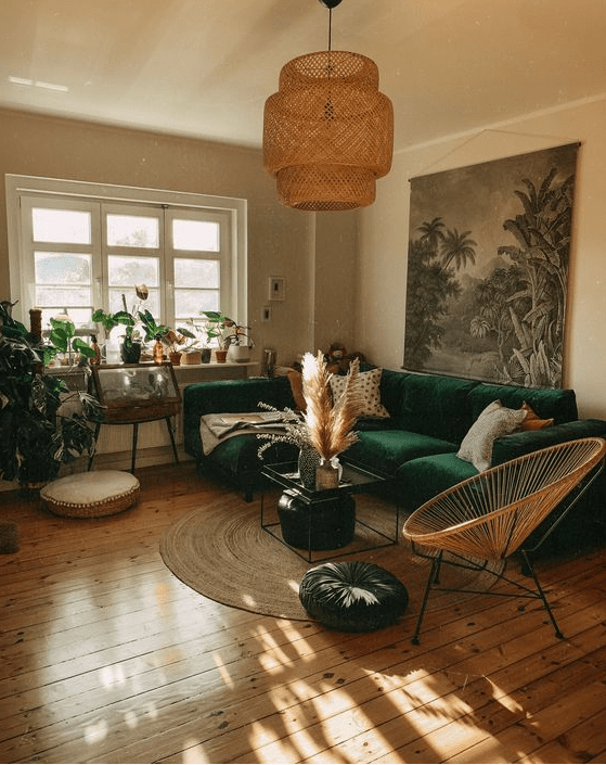 A cool boho living room with a bold green seating area, a coffee table, a round chair, potted plants, some art and pampas grass