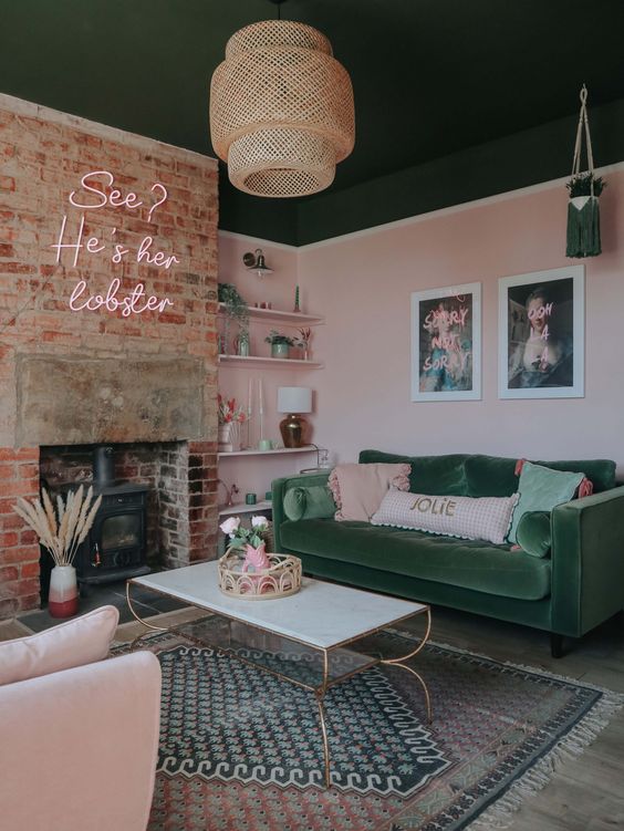 a pink and green living room with a dark green ceiling, a brick fireplace with a hearth, a green sofa and a pink chair, and layered rugs