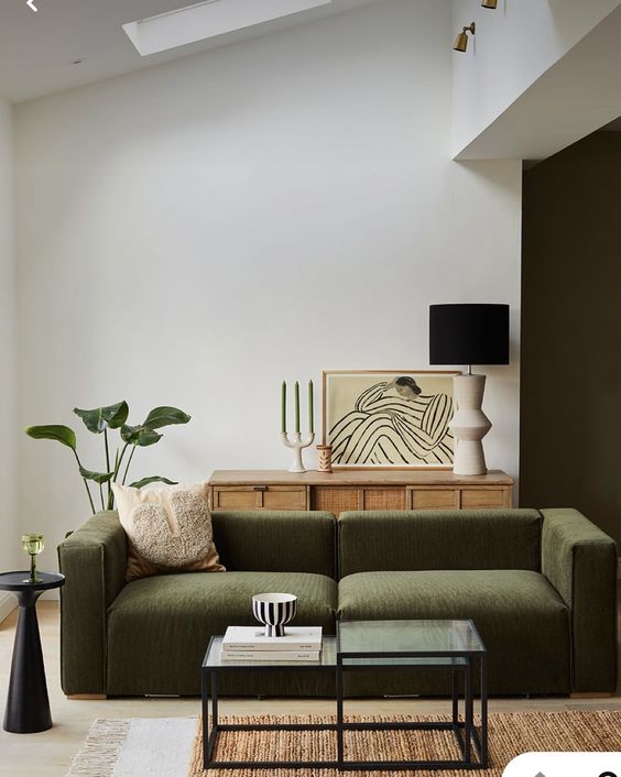 a sophisticated modern living room with a low green sofa, a cane sideboard, a glass coffee table, lamps and green plants