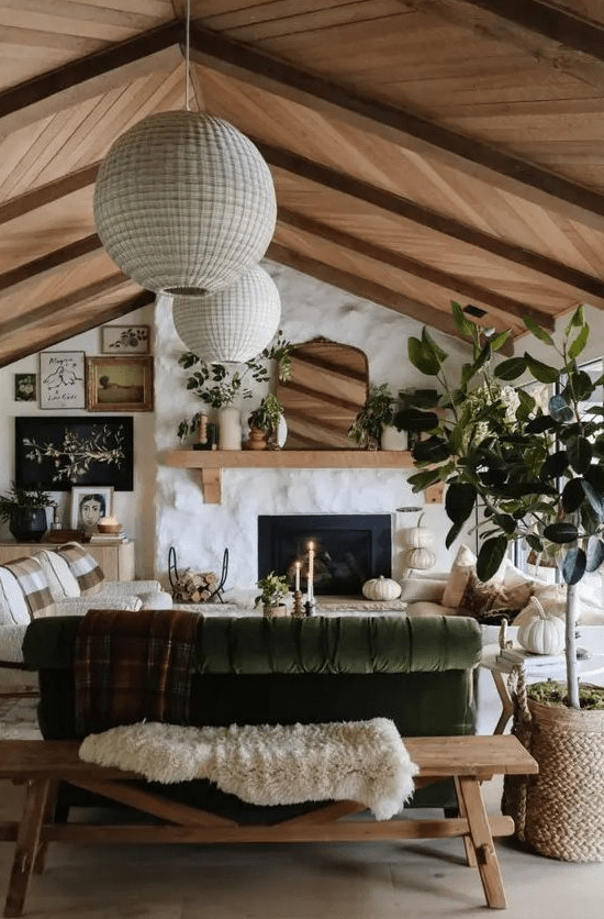A welcoming, neutral and earthy room with white stone walls, white chairs and a green sofa, a fireplace and a sloping wood-clad ceiling