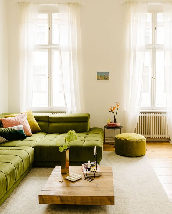 an airy living room with a low green sofa, a low coffee table, a stool and a side table and colorful cushions