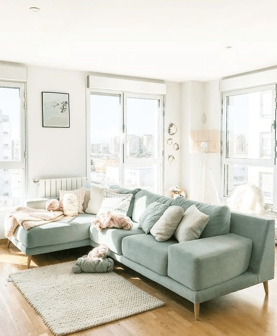 an airy living room with light green sofa sets and neutral pillows, a rug and some green wreaths