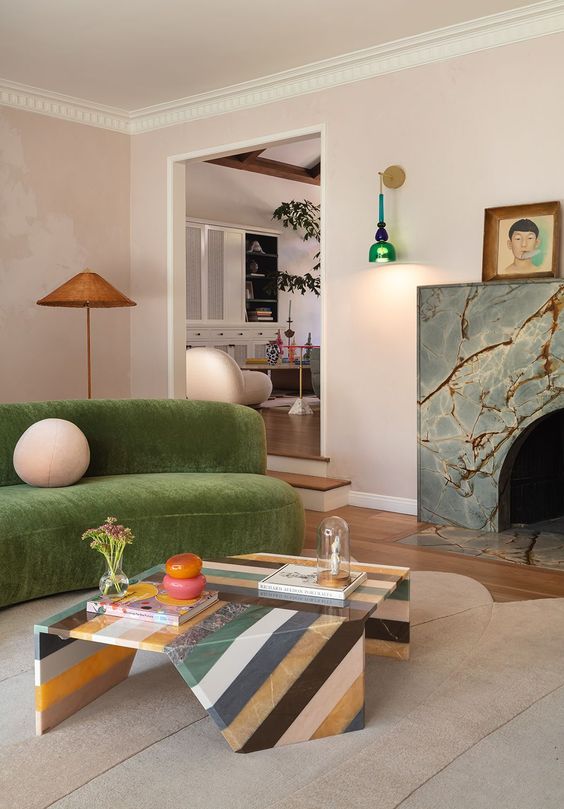 a whimsical living room with a stone fireplace, a green curved sofa, a striped stone coffee table and bright and cool decor