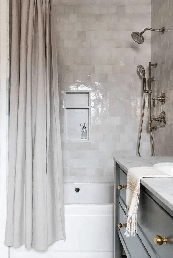 a chic, modern bathroom with light gray and neutral zellige tiles, a neutral shower curtain and a black vanity