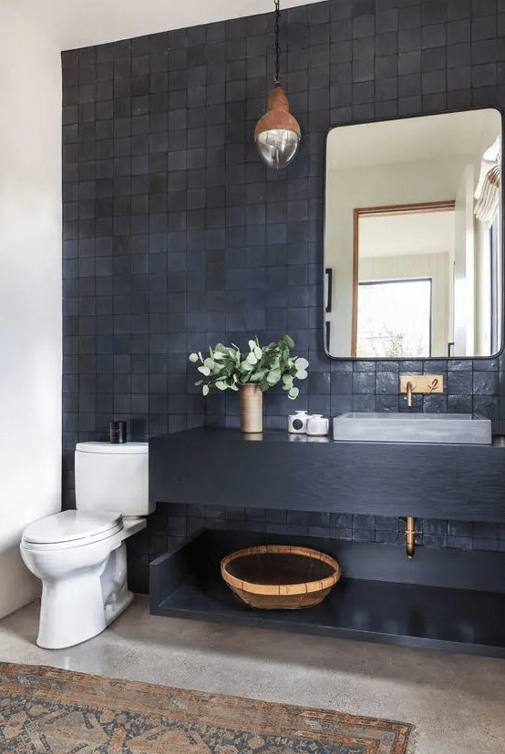 a modern bathroom with gray and black zellige tiles, a black floating vanity and shelf, a mirror, a statement pendant lamp and some decoration