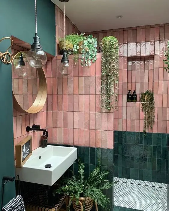 a bold green and pink bathroom with stacked thin zellige tiles, a shower area, sink, potted plants and pendant lamps