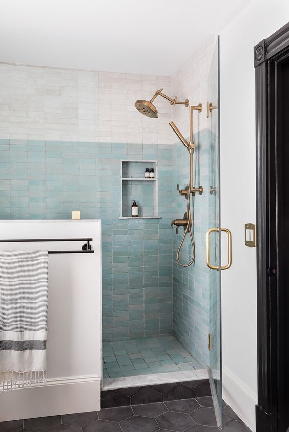 A large shower area clad in white and aqua thin zellige tiles, brass hardware and a niche shelf is amazing