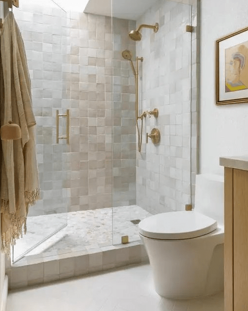 an attractive and light-filled neutral bathroom with neutral zellige tiles, a skylight over the shower, white appliances and gold fixtures